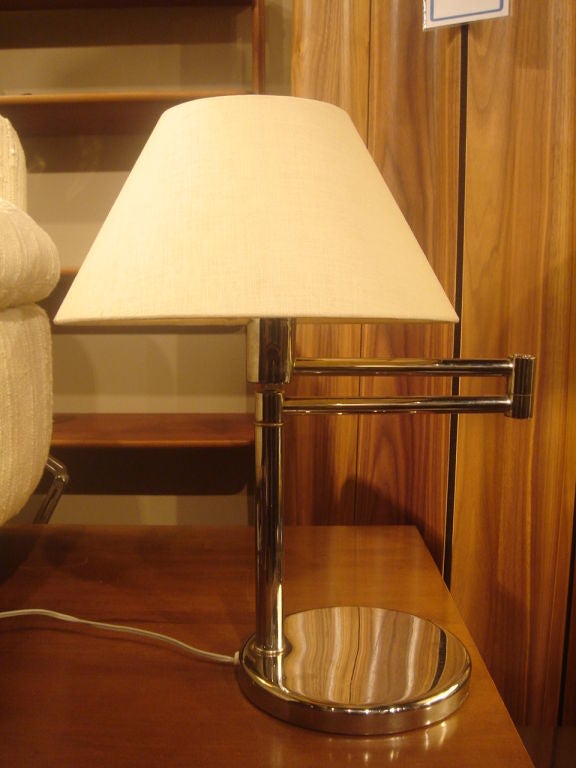 Swing arm desk lamp in chrome lamp by Nessen Studio. USA, circa 1970.<br />
<br />
Round base with swing arm in mirro chrome finish.  Complemented by a linen lamp shade in ivory.<br />
<br />
Priced as a single lamp; a pair is also available.<br