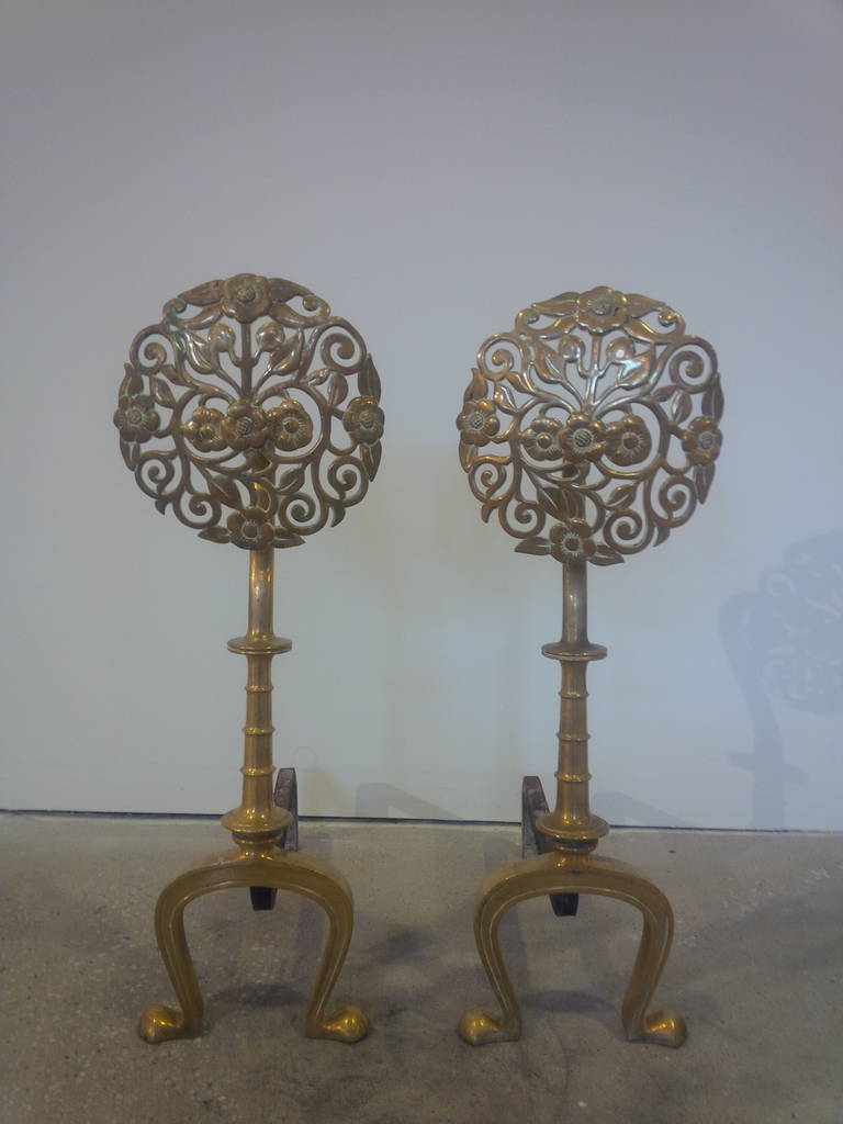 Pair of polished brass andirons with a floral-patterned, sunburst style design.  USA, circa 1940.