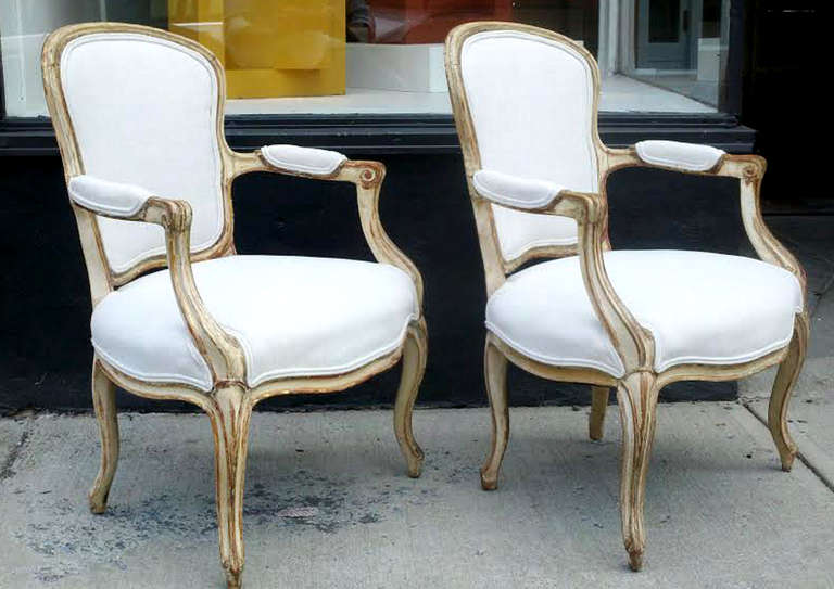 A pair of comfortable exemplary French Rococo armchairs/bergeres (fauteuils a la reine). Painted and parcel gilt wood frames with car-touche-shaped padded seat backs, padded arms, serpentine rails and cabriole legs. Fine fluid wood-carvings, loose