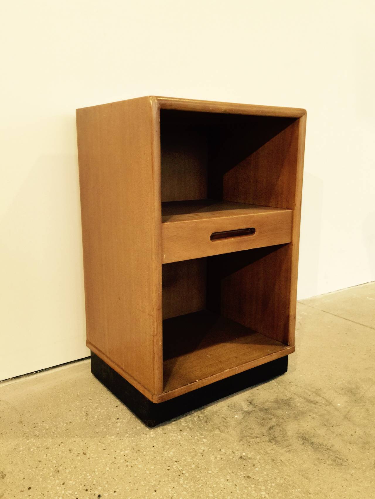 Mahogany nightstand with black leather-wrapped base by Edward Wormley as part of the New World collection for Dunbar, USA, circa 1950. 
Features single center drawer with inset handle with a shelf above and below. 
Retains original bleached mahogany