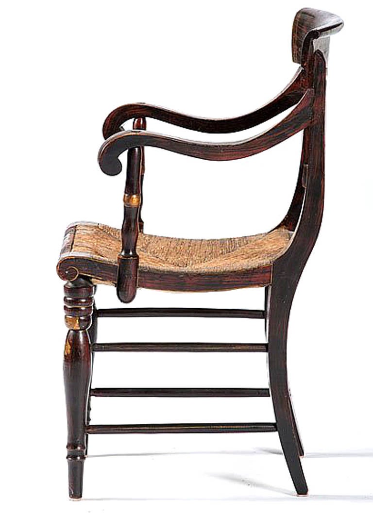 This American 19th century, stencil-decorated armchair features fruit and flower motifs over a rosewood grain painted finish, having a beautiful crest rail, rush woven seat, scrolled arms, and ring turned tapering legs connected by ring turned