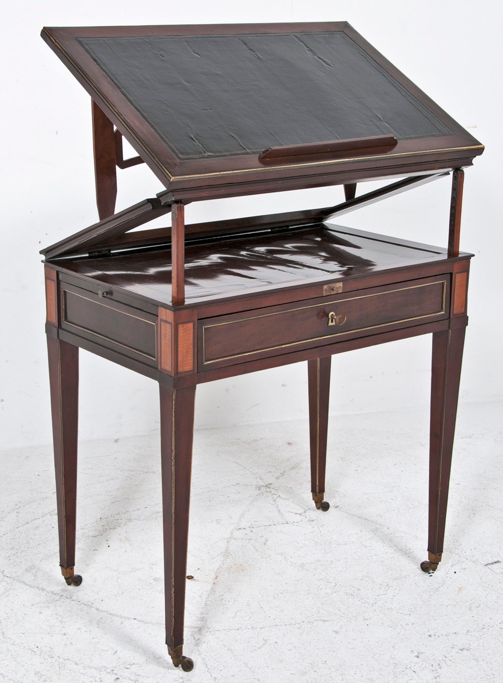 This elegant small and useful architects desk was made in the area around the Baltic Sea early in the 19th century. The top is inlaid with leather. The case mostly mahogany but with satinwood and brass inlays. The top raises and tilts depending if