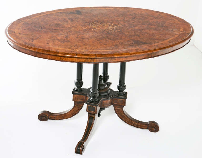 A surprisingly nice inlaid walnut Victorian period oval loo or breakfast table. The top is richly veneered with burled walnut and inlaid with geometric boxwood stringing. The top supported by four ebonized columns. Standing on four out swept legs. A