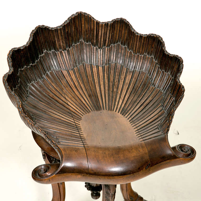 A whimsical and useful stool.  The seat carved as a large shell supported on three scrolling lion paws feet on a tripod base.  The seat rotates and has a wonderful lightly worn surface along with some shrinkage.  We think this was made in Italy late