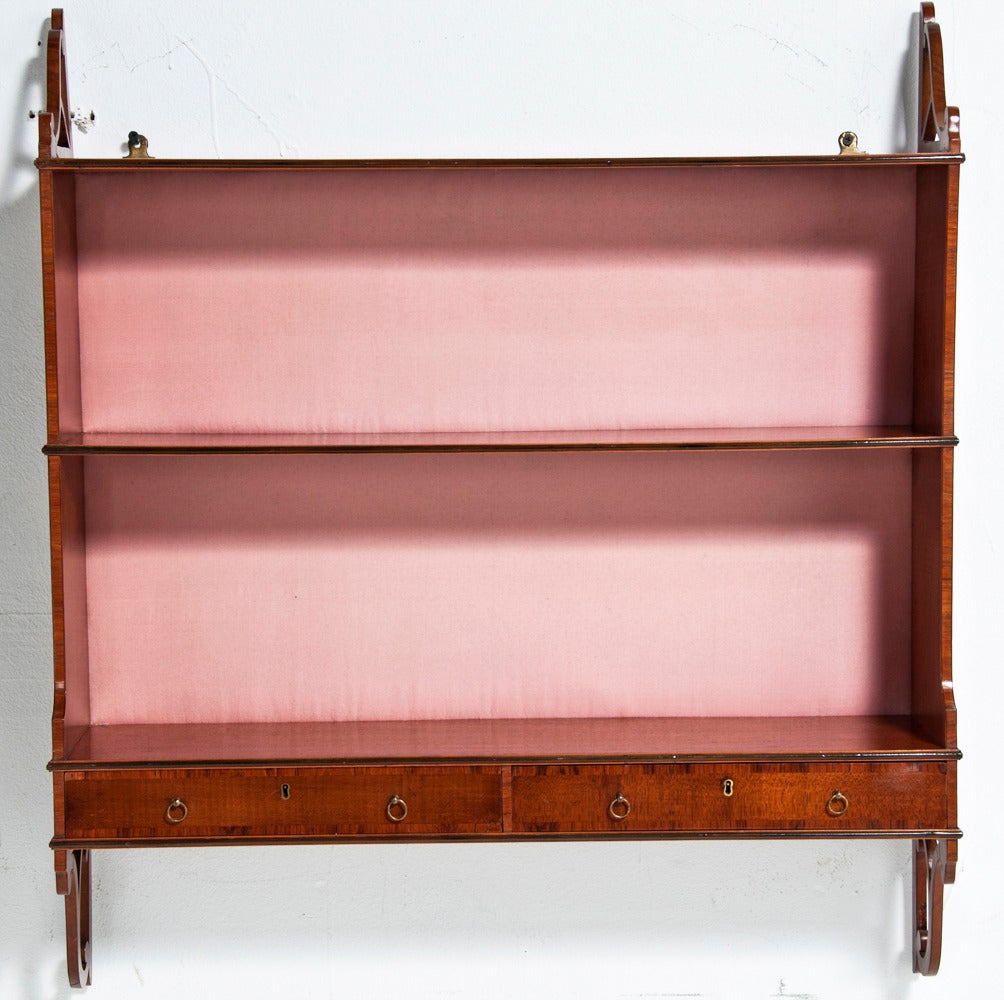 A very elegant and restrained George III period partridge wood hanging shelf with two drawers made in England about 1800 in the Sheraton manner.   A rare useful and small piece.  The peach satin back is a later covering.   It could be easily redone