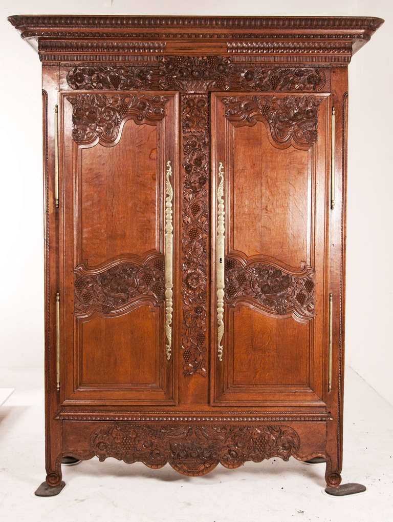 An early 19th century French marriage armoire with a basket of flowers and grapes on the tops of the doors. The front apron is carved with a basket of flowers flanked by a pair of love birds, which symbolize marriage. The door faces have carvings of