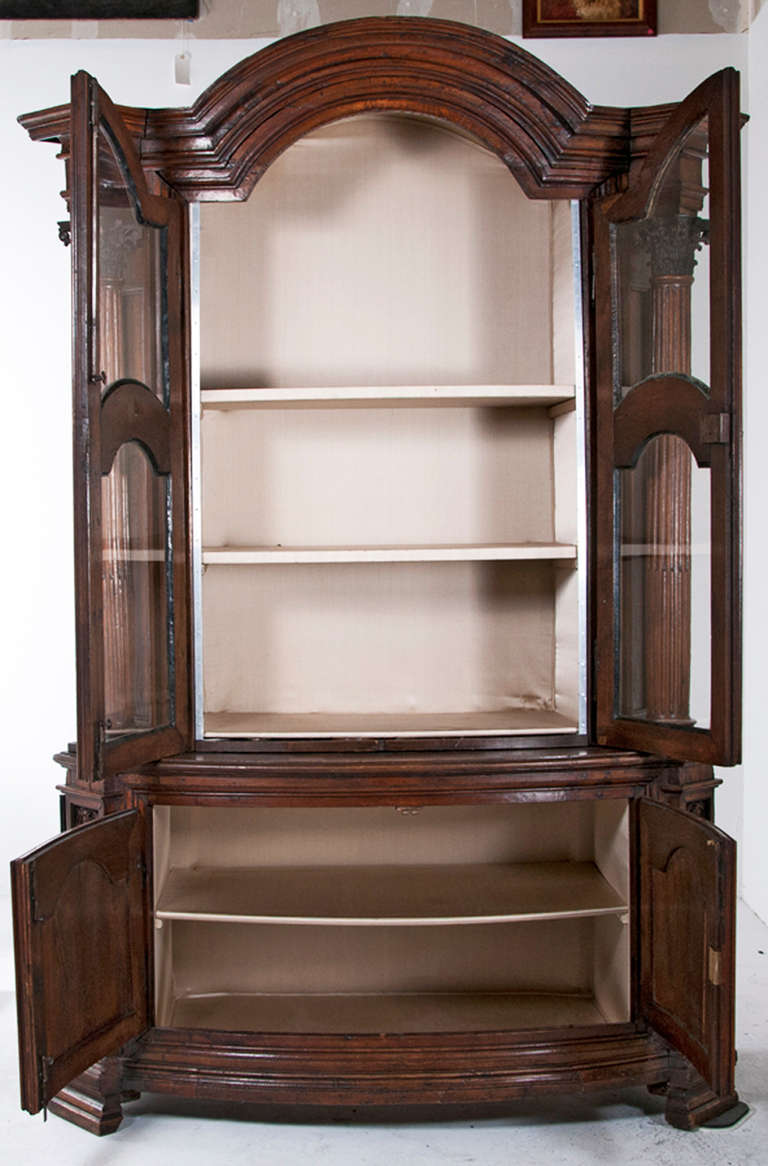 A 18th century Northern Italian or Southern German oak cabinet. The upper section, with curved glass doors and side doors with glass panels added in the 19th century. The bottom section has two doors in the front and both bottom side panels open for