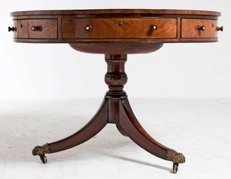 A mid 19th century English mahogany rent table with a burgundy leather inset top. There are six drawers, three open, three are fixed. The table is on a pedestal with three sabre legs terminating in lion paw casters.