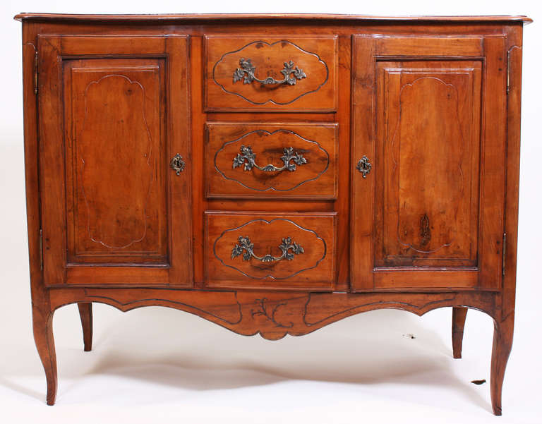 A 19th Century Continental fruit wood buffet with a wonderful carved floral in a cartouche on each side panel. 2 cabinet doors flanking 3 drawers. One back leg replaced.