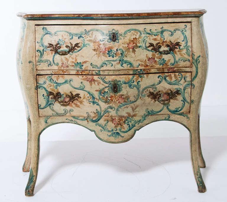A pair of Midcentury Italian painted bombe commodes in the Louis XV Style. The front and sides are painted in a wonderful warm cream color with sprays of flowers in blues and rusts, the top is a faux painted marble.
