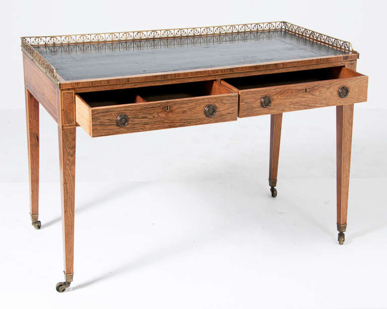 A rare and unusually high quality Regency Period faded rosewood writing table with boxwood stringing and a gilt brass rail.  This piece was made in England about 1820 and appears to have original leather top.  Finished on all four sides this piece