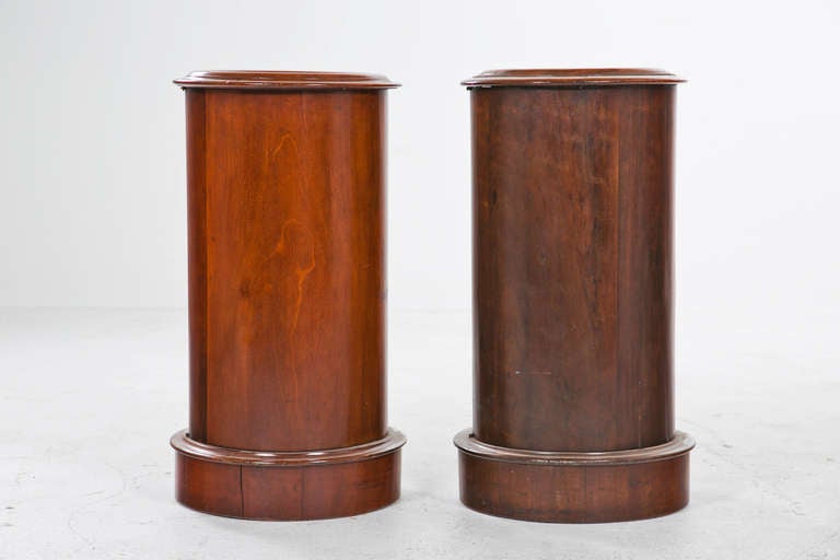 A nice assembled pair of English mahogany pedestal cabinets with inset marble tops.  The brass knobs are later.  Wonderful bedsides, these are great as  pedestals or plant stands.  Chic useful classics very hard to find in similar sizes and colors. 