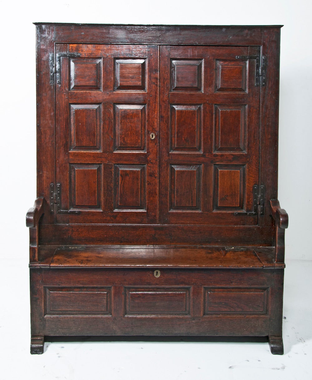 English early 18th century oak bacon settle, circa 1720 of superb color and condition. The field panelled doors open to reveal original iron hooks and three later shelves. The back has ventilation holes. Typically the doors are on the back side.