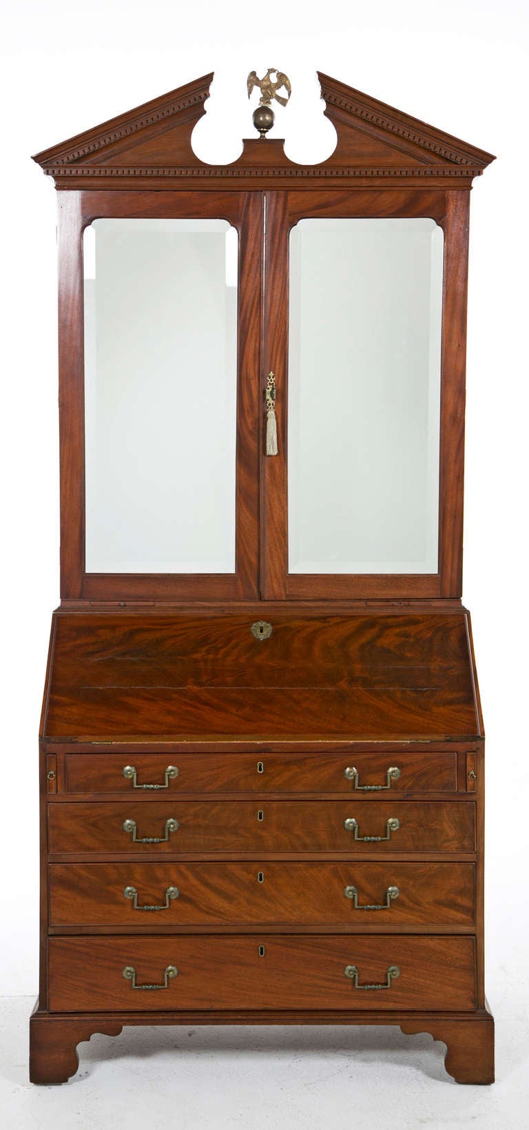 An Georgian secretaire or bookcase made in the United Kingdom, late in the 18th century standing on ogee bracket feet with mirrored top doors and drop front revealing fitted drawers and pigeon holes for sorting. Nice brass pulls on four graduated