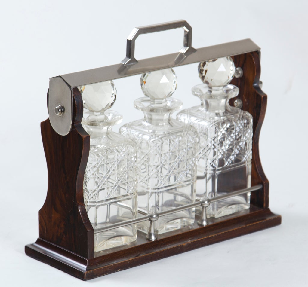 A handsome antique English decanter set of three cut crystal bottles and stoppers in a locking rosewood frame with metal mounts.  A great present for someone with teenagers.