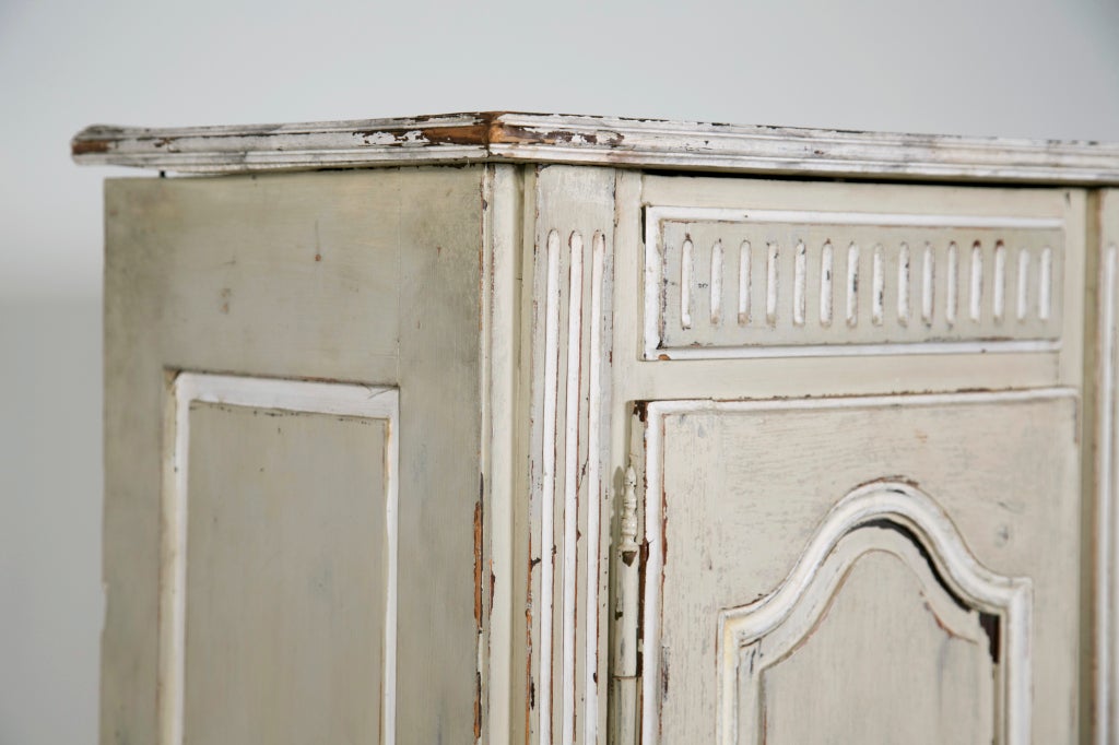 A charming small scaled Swedish grey and white cabinet with four doors and shelves. This piece has a nice shallow profile. Good carving and an interesting older surface. At some point the base was restored / possibly replaced. Originally this piece