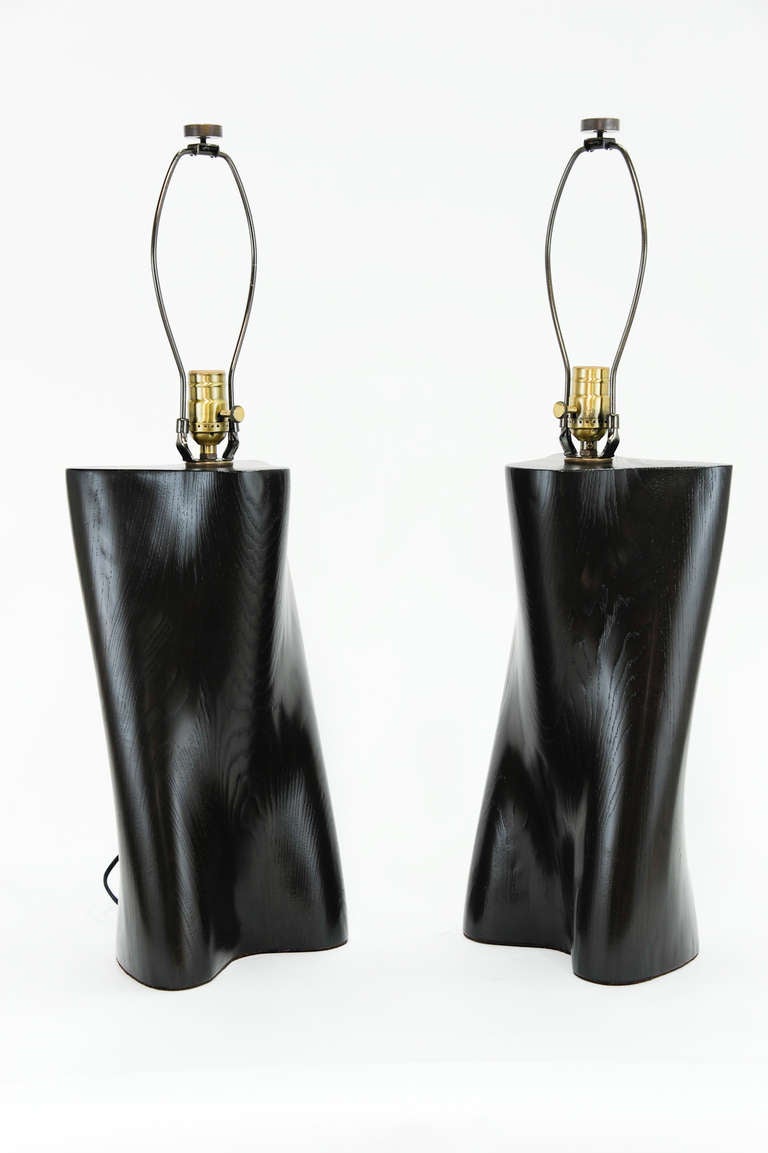 A wonderful pair of hand-carved table lamps. Lamps have been completely refinished and rewired. They are a dark black with a translucent lacquer finish that shows the graining of the wood. We have acquired a large number of these lamps and can fill