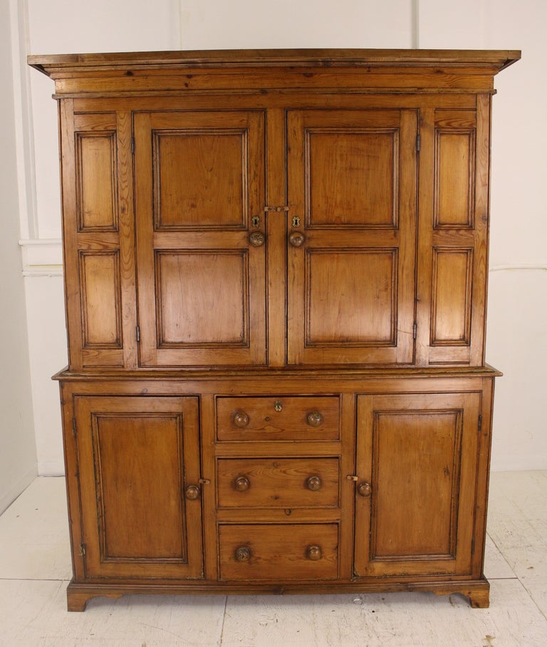 Gorgeous in color and patina,  in Georgian style and of museum quality.  The raised fielded panels, strong cornice, charming shaped apron, a classic arrangement of drawers between doors on the bottom half of the piece. Very nice original brass