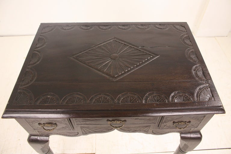 A lowboy from England. Wonderful legs and strong  pad feet. The carving with a scallop and diamond pattern was done later, a frequent practice, probably from the Victorian era. In classic dark oak.  Three small drawers with replaced handles. A good