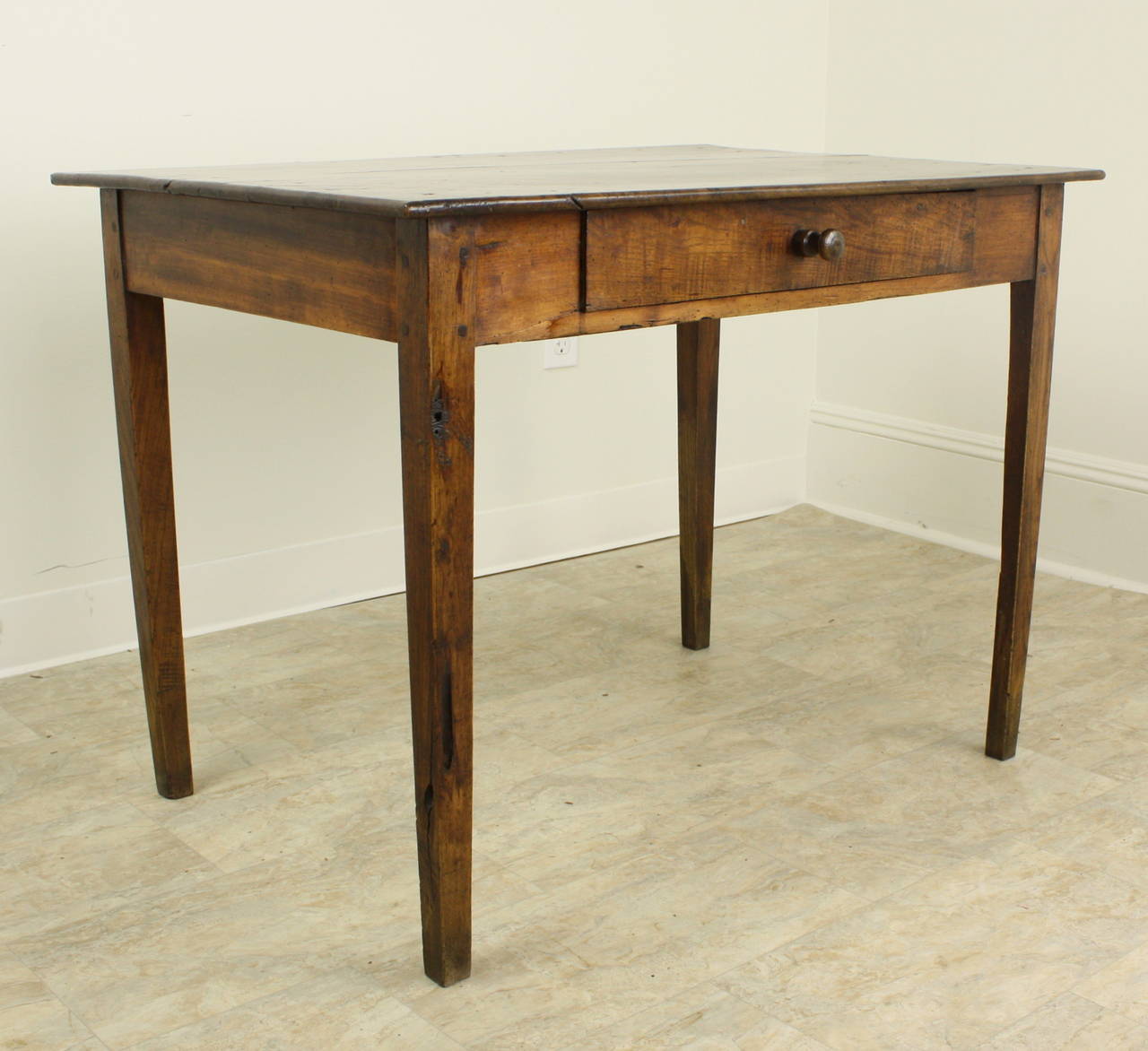 A beautiful antique cherry color, grain and patina.  With long slender tapered legs, the base of the table has a drawer in the apron, with the proportions providing a lovely French country table look.  The table is the perfect height for a lamp, and