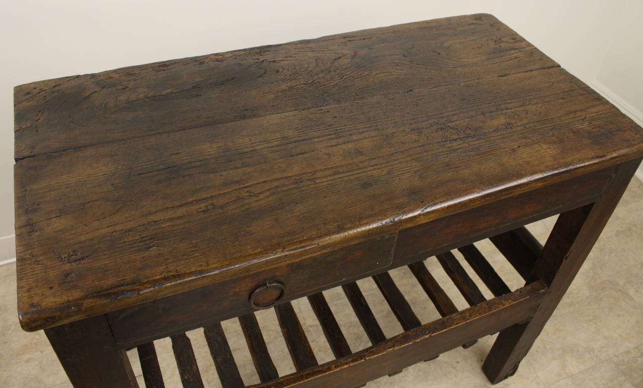 Old dark chestnut, with lots of wear, this is a great pantry or kitchen piece. Lovely wood, nice and chunky, with a drawer in the apron with a hand wrought pull. The slatted base is similar to early bread drying racks. This table would be a very