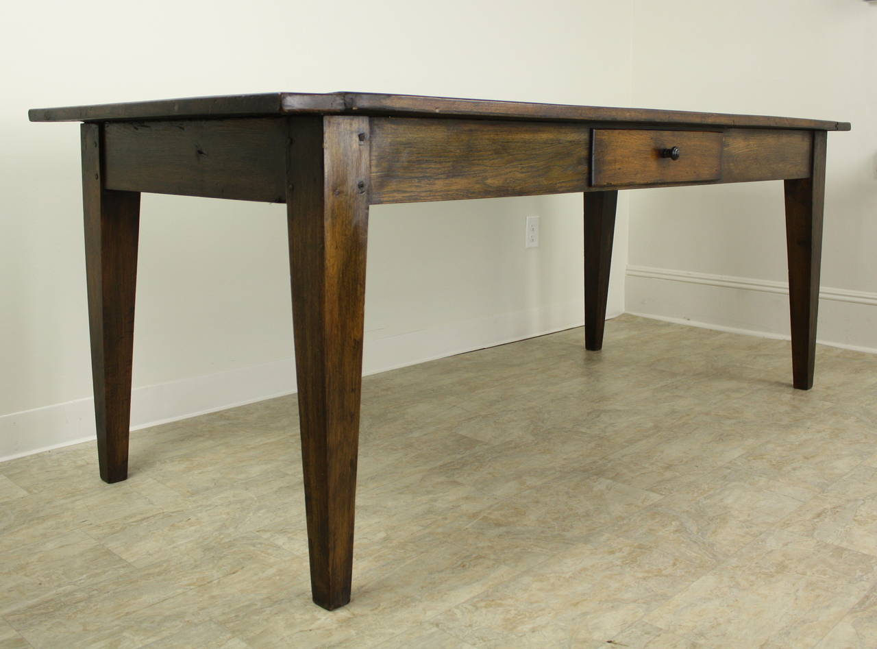 This is a very desirable dining table, having many classic attributes of the French farmhouse table.  There is one center drawer on a long side, slender tapered legs positioned near the end of the top to maximize seating between the legs. Color is a