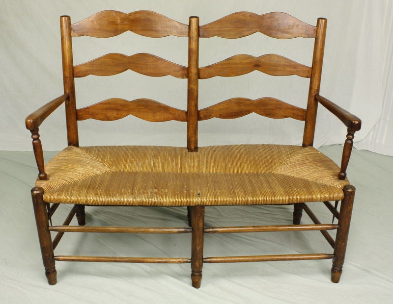 Charming. A very pretty and sturdy antique bench from France, with a rush seat. Seats two comfortably. Cherry is a warm color with nice patina.

See similar examples of antique French benches on our website www.BriggsHouse.com. 

Briggs House,