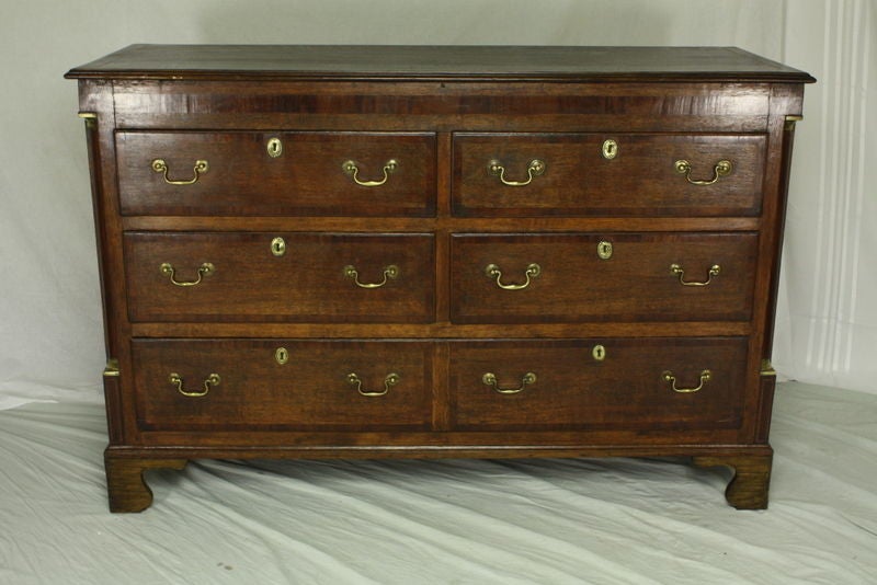 An antique oak chest of drawers from England. Very decorative with cross-banding on the drawers, the top, and the frieze as well as columns on the side with lovely brass tops and bottoms,   with inlay below. Panels on the sides. The oak has a rich,