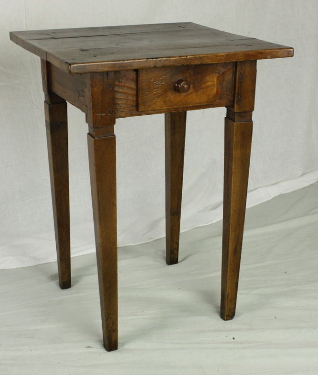 An antique side table from France with one small drawer and an unusual square top. The decorative cut out at the top of the legs is distinctive. Made of cherry wood with wonderful grain and a rich patina. The top has some old ink marks which add to