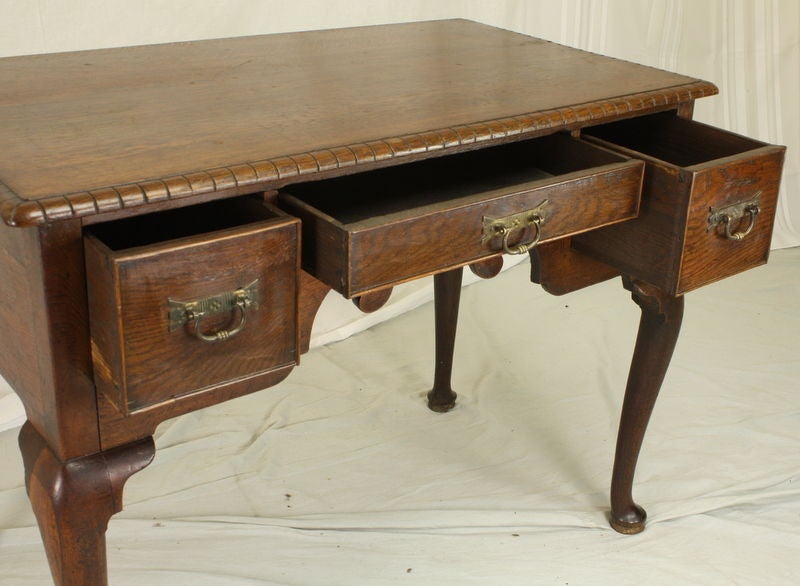 An antique pad foot lowboy from England. Three cockbeaded drawers with very pretty old brass. Note the elaborately carved apron and the unusual carved edge to the top. The oak has a rich and warm color. With a width of 39