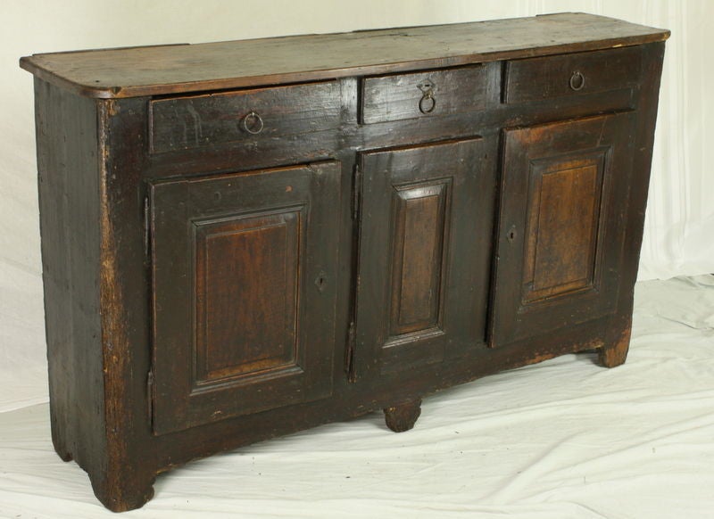 An antique pine enfilade from France. Very rustic and very charming! The pine has a deep stain and is rich in wear and patina. Original escutcheons and hinges on the cabinet doors and round iron pulls on the three drawers. Base has a two/one