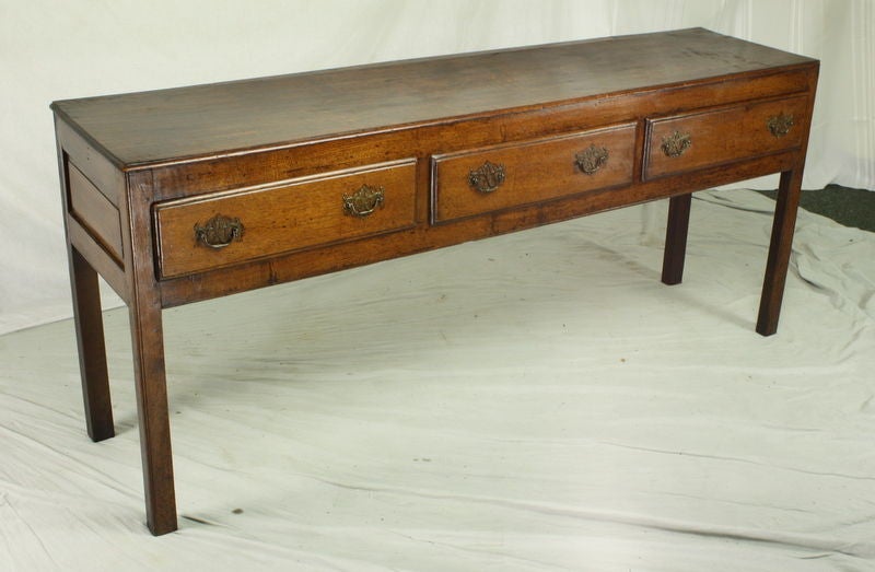 An early English oak three drawer console with a simple elegant silhouette.  The oak has a beautiful grain and color. The straight legs and brass drop handles with Georgian backplates complete the look of this sideboard. Would make an arresting hall