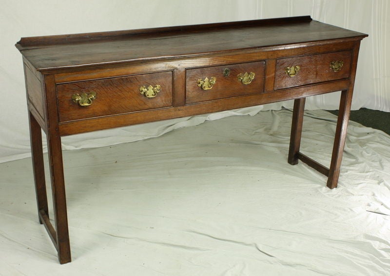 A gracious period three drawer oak console with a galleried back and rail supports on the sides.  Fabulously grained drawer fronts and extravagant brasses add to the look of this sideboard.  Each roomy drawer is 18