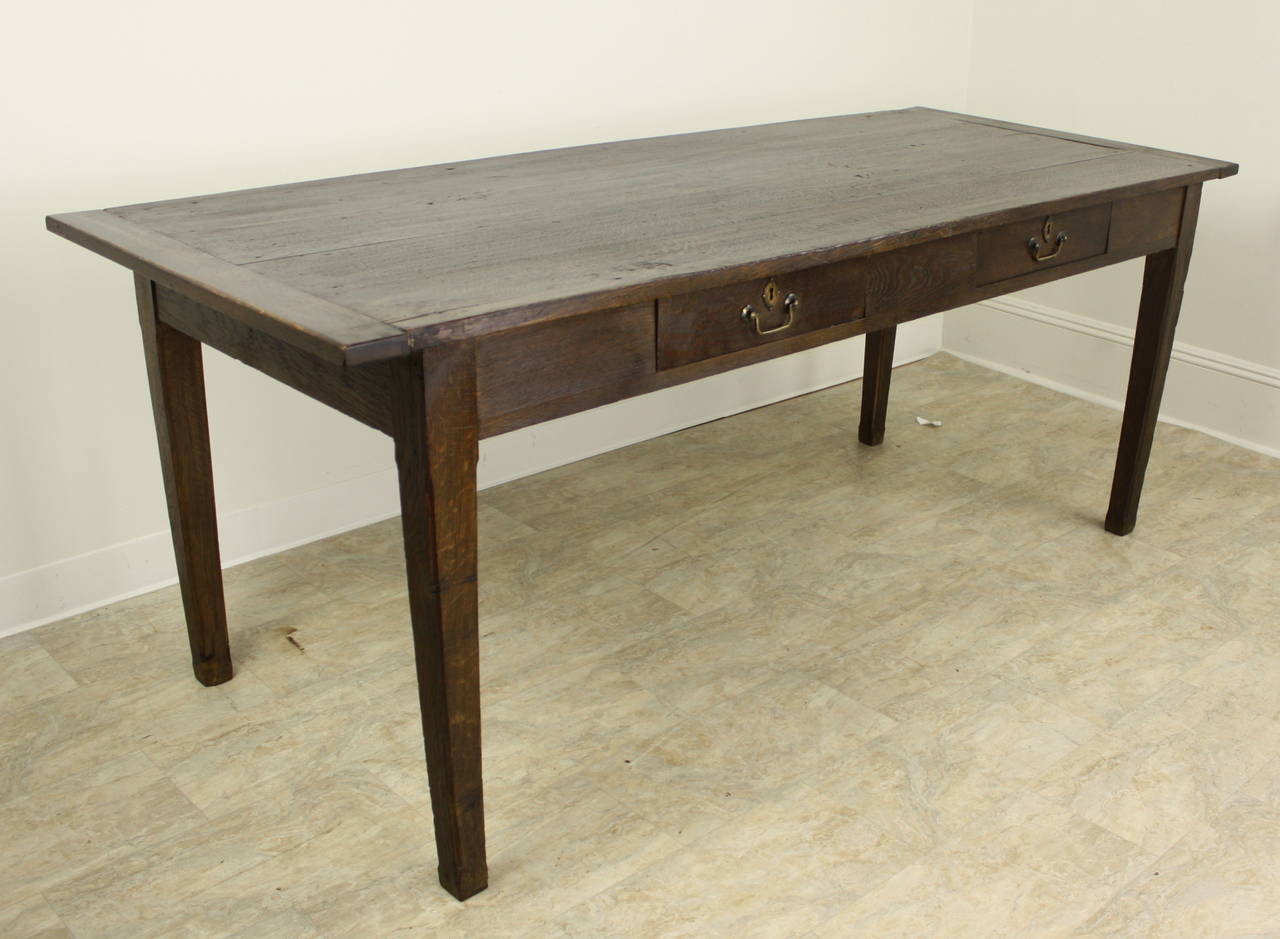 A dark chestnut country farm table with nice decorative details including breadboard ends and two drawers on one side.  Solid and sturdy with moderately tapered legs and deep rich color and patina. Apron height is good for knees at 24.5.  Distance