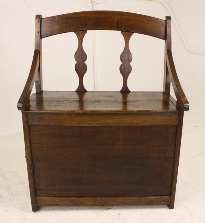 Delightful, very charming French chestnut fireside seat. The main feature is the unique little cupboard, with a raised-panel door, and a little round knob, on one end of the seat. The bench has shaped back and vertical supports, and lovely sloped