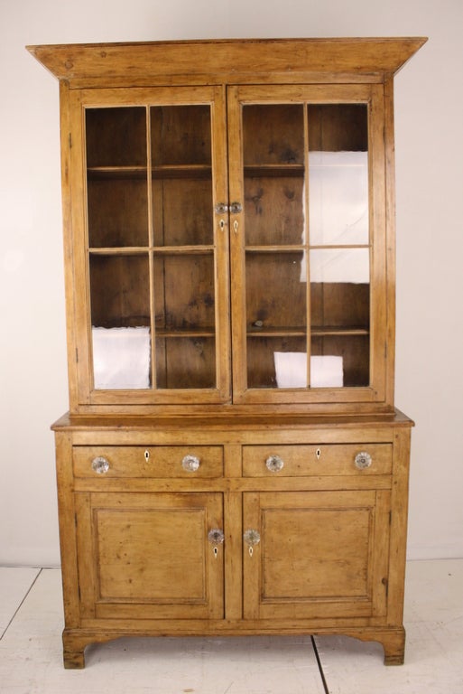 The pine on the cupboard is a very pretty warm honey color, which comes from age. With the bookcase or display case top, two drawers and good size storage behind the two doors, the piece has a lot to offer. Top and bottom are in separate pieces.