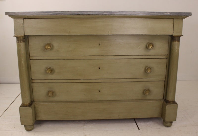 Very chic bureau. This commode is a Classic Empire chest of drawers, with round beautiful and graceful vertical side columns, and bronze pulls on the drawers. A complimentary lighter gray marble is lovely with the enhanced old green paint. Columns