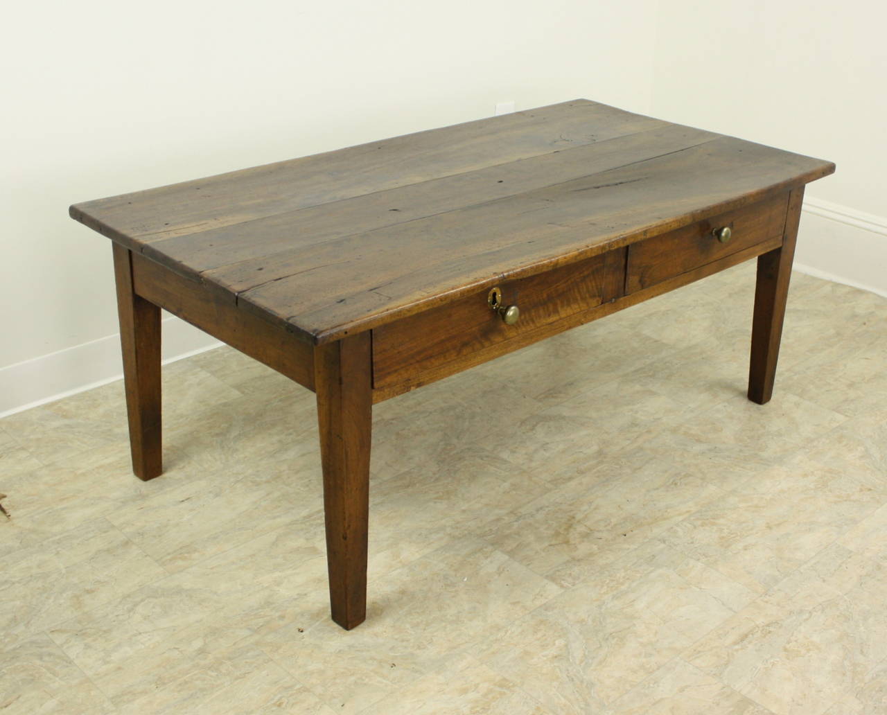 A handsome silhouette in well grained walnut.  The top has dramatic color and lovely patina.  Two drawers at the front, including a hand wrought key hole,  add an interesting design note, The gently tapered legs are sturdy, and add to the overall