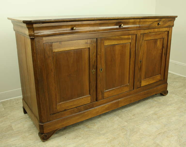 A Louis Philippe long buffet with an additional decorative touch--this sideboard has very pretty hand-carved scrolls adorn the two front feet. Canted corners at the top, and three drawers over three doors offer good storage space.  The walnut grain