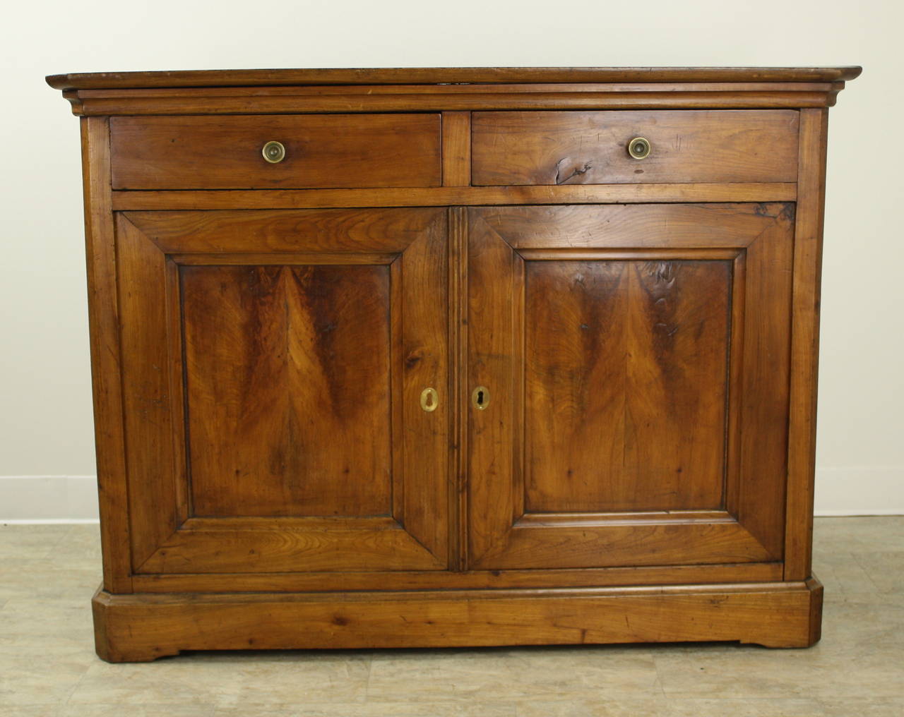 A smaller, slim cherry buffet with marvelous dramatic grain, especially on the inset door panels.  Elegant and simple in the Louie Philippe style.  Two bottom doors open to a roomy storage space with a single shelf.  Top has nice contrasting colors
