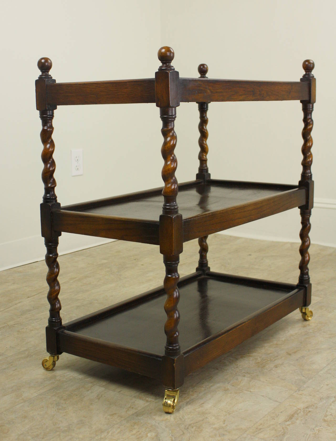 Charming three-tier bar cart. Rich dark oak, with decorative barley twist legs with small rounded tops. Original castors. There are 9.5