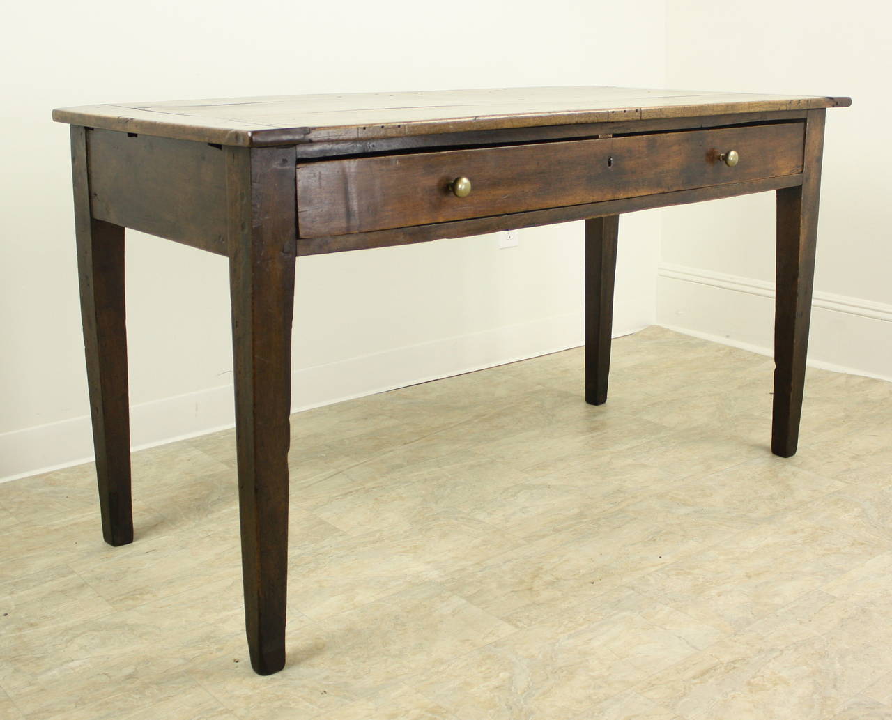 A generously proportioned writing table or desk with lovely grain and nice patina.  The top shows interesting distress appropriate for the age of the piece.  One long drawer accented with pretty brass knobs.The 24