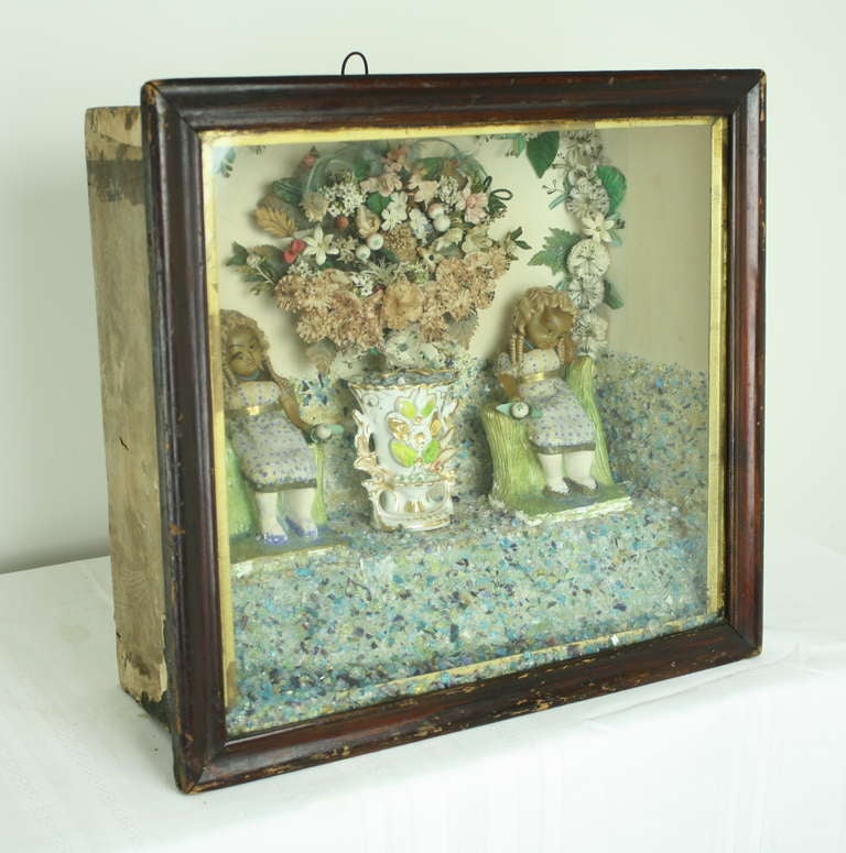 Very detailed and clearly lovingly made antique English folk art piece.  Very creative use of glass bits for base, use of porcelain Victorian vase, dolls are sitting in ceramic seats.