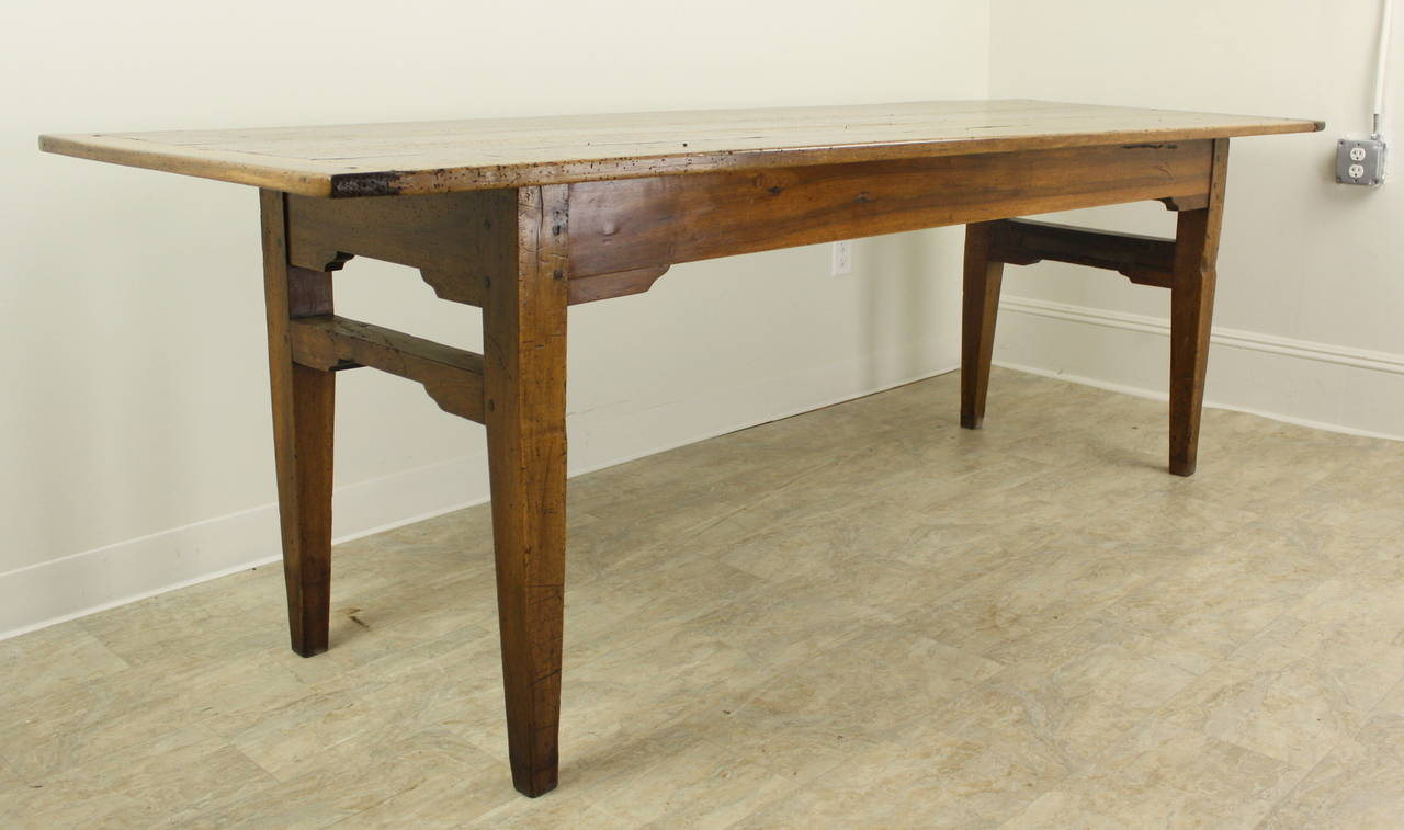 An utterly charming long farm walnut farm table with dramatic grain and fanciful detailed stretchers between the legs at each end.  Along with breadboard ends, the top has some interesting distress including a natural knothole, pictured in image #6.