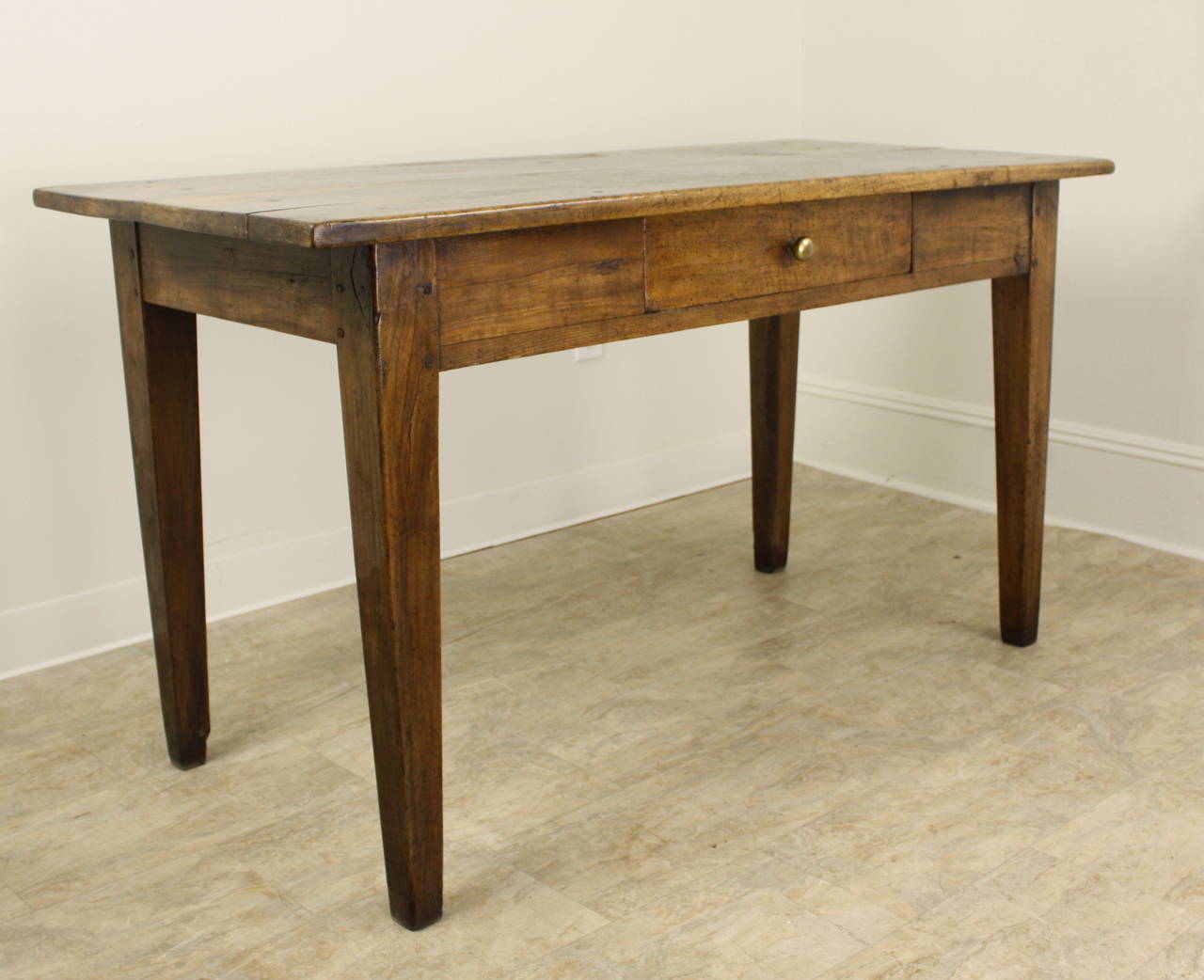 A generously proportioned writing table or desk with lovely grain in well patinated walnut. The top shows interesting distress appropriate for the age of the piece. One drawer accented with pretty brass knob. The 24