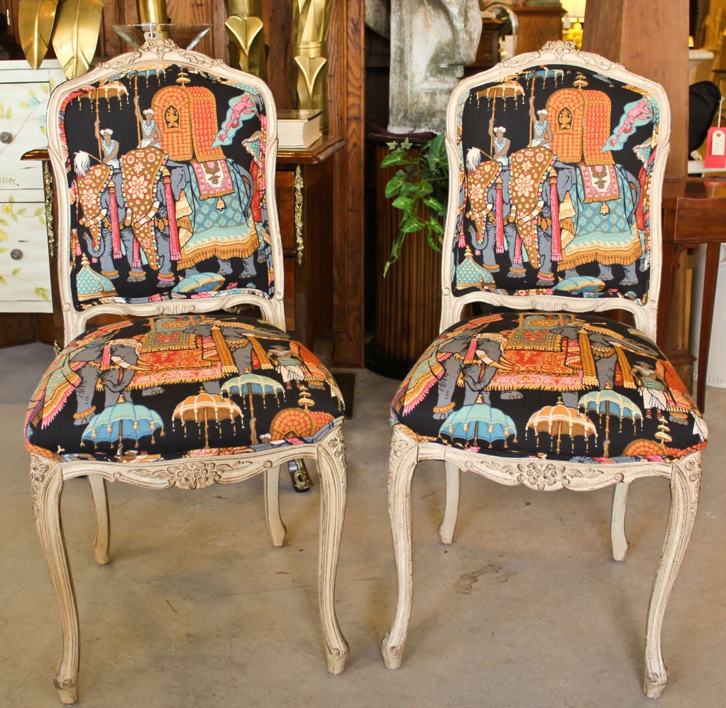 A pair of nicely carved and painted Louis XV style side chairs. The painted antiqued finish is a darker bone color with highlights. They are newly upholstered in a very chic and expensive heavy linen. The fabric depicts an Orientalist fantasy scene