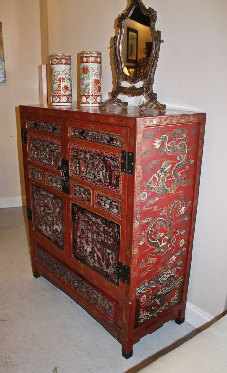 A red laquered Chinese 2 door cabinet with carving and gilding on front panels.