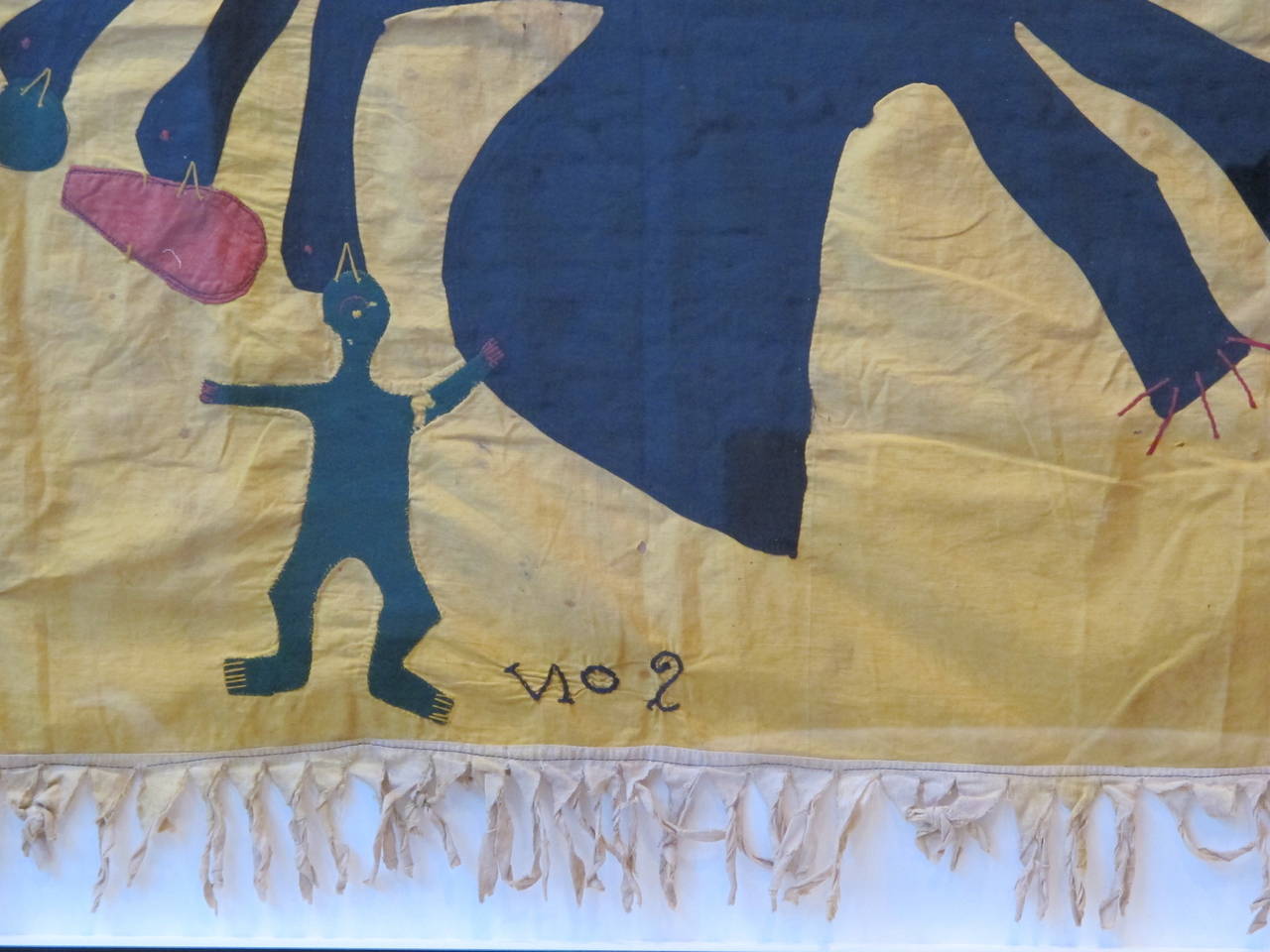 Yellow cotton patchwork Asafo flag with ivory cotton header and fringe, featuring a naive applique of a dragon eating several green men and a red trumpet. The flag has been hand-stitched to acid-free board, in a black painted wood frame under UV