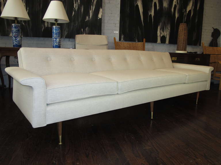 Long 1950s sofa with back tufted with square buttons, on walnut tapered legs with brass sabots. Newly recovered in natural linen.