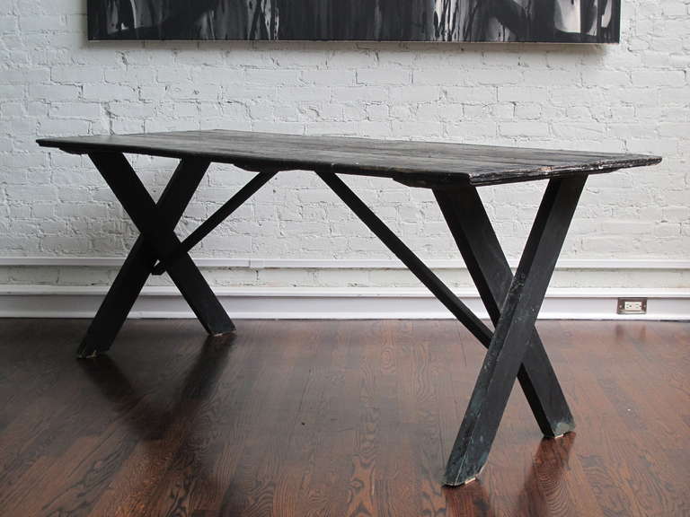Black-painted pine farm table with trestle base. Paint is worn to reveal earlier coats of green and white paint, as well as pine. Table top is fashioned from an earlier tongue and groove door. Would work well for dining indoors or outdoors, dining